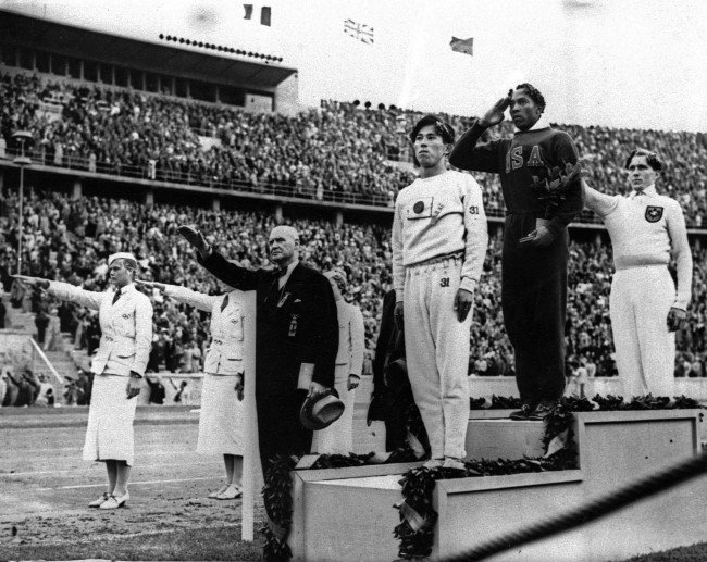 FILE - In this Aug. 11, 1936 file photo, Olympic broad jump medalists salute during the medals ceremony at the Summer Olympics in Berlin. From left on podium are: bronze medalist Jajima of Japan, gold medalist Jesse Owens of the United States and silver medalist Lutz Long of Germany. Long and German Olympic officials give the Nazi salute, while Owens gives a traditional salute. It is 