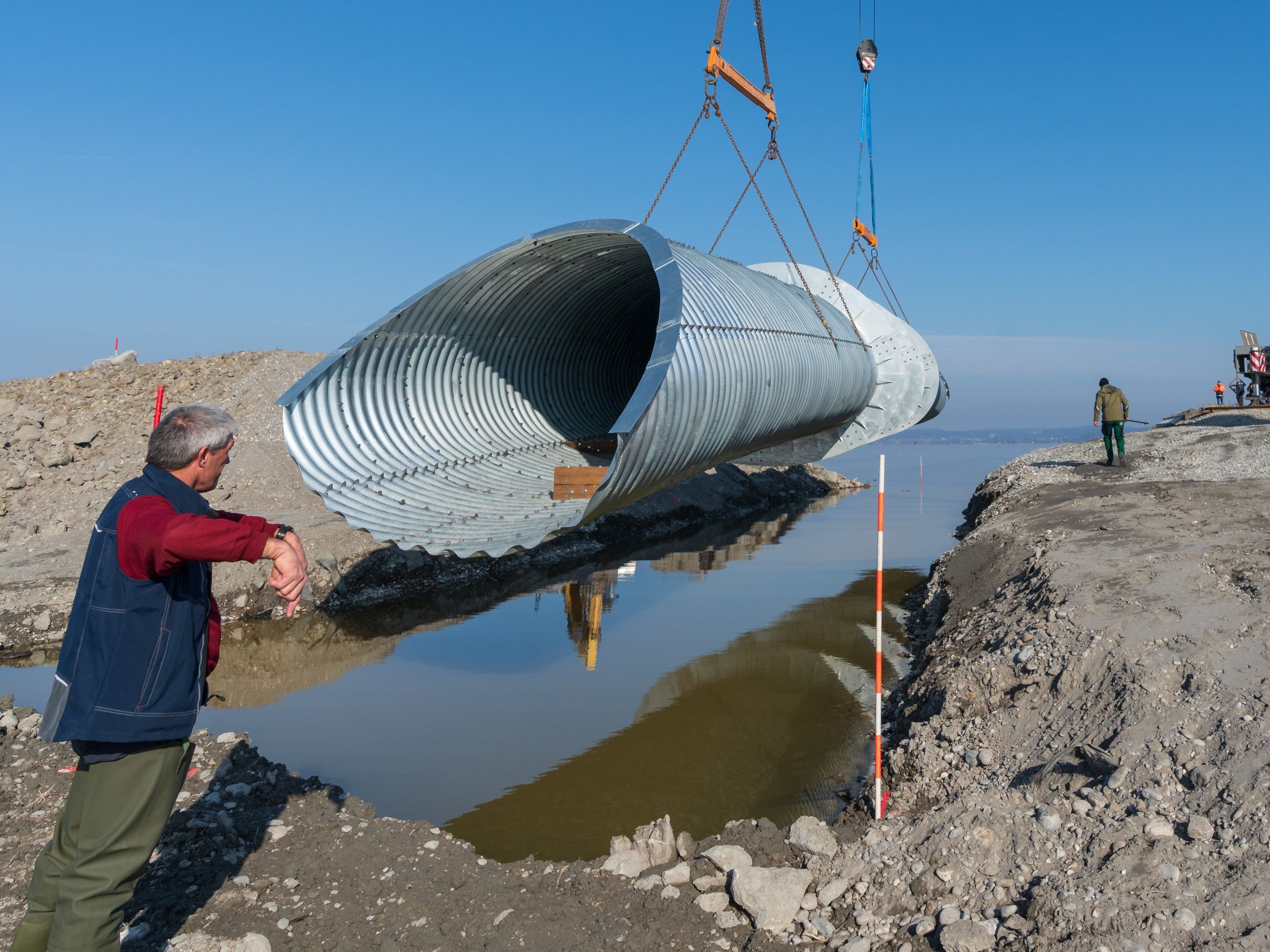 Mit zwei Telekränen wurde die Fischunterführung in das zuvor ausgebaggerte Loch am Rheindamm eingehoben. Mit zwei Telekränen wurde die Fischunterführung in das zuvor ausgebaggerte Loch am Rheindamm eingehoben.