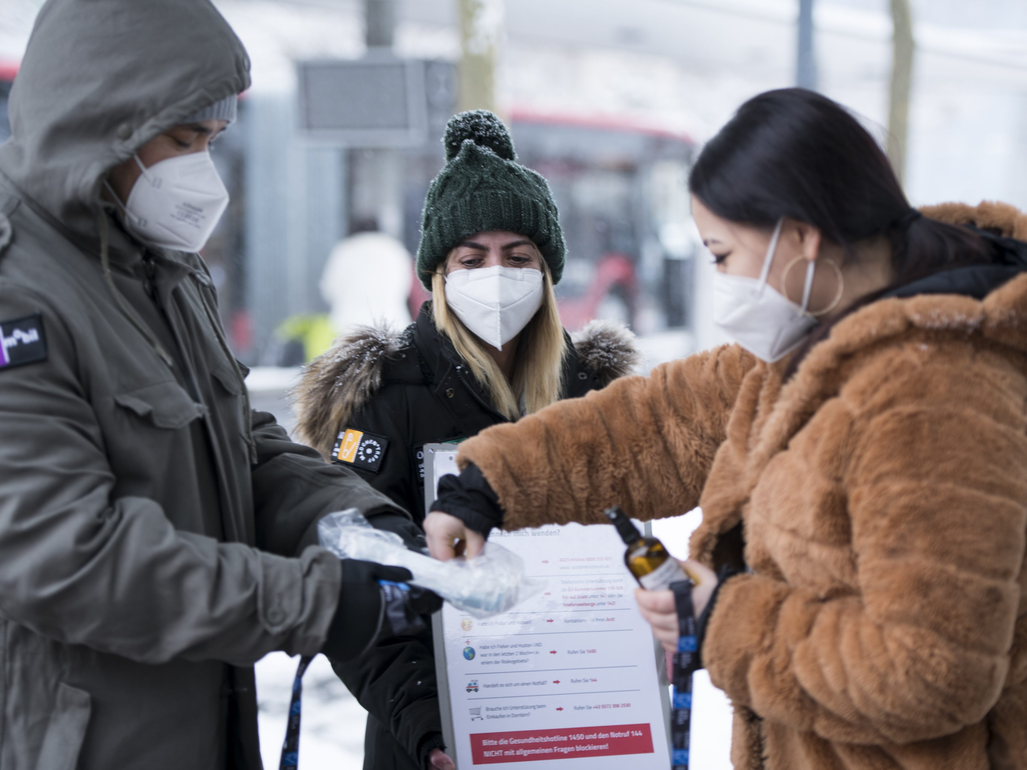 Ali Khavari und Yasemin Polat mit einer Jugendlichen beim Ausgeben von Desinfektionsmittel und Masken am Bahnhof Dornbirn.