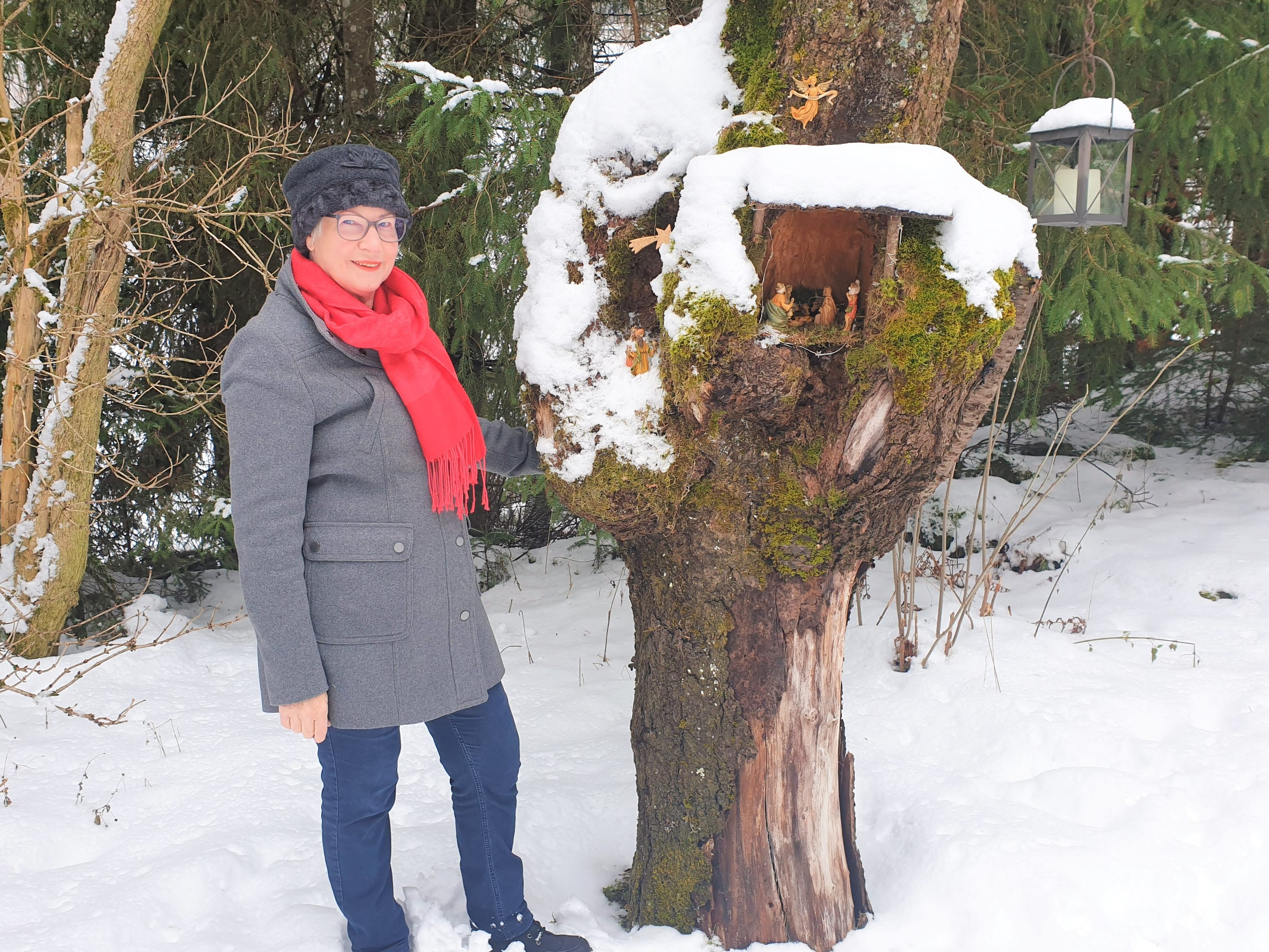 Marlies Kuster, die gute Seele des Krippenbauvereins, steht hier vor einer Krippe, die in einem Baumstamm eingebettet ist.