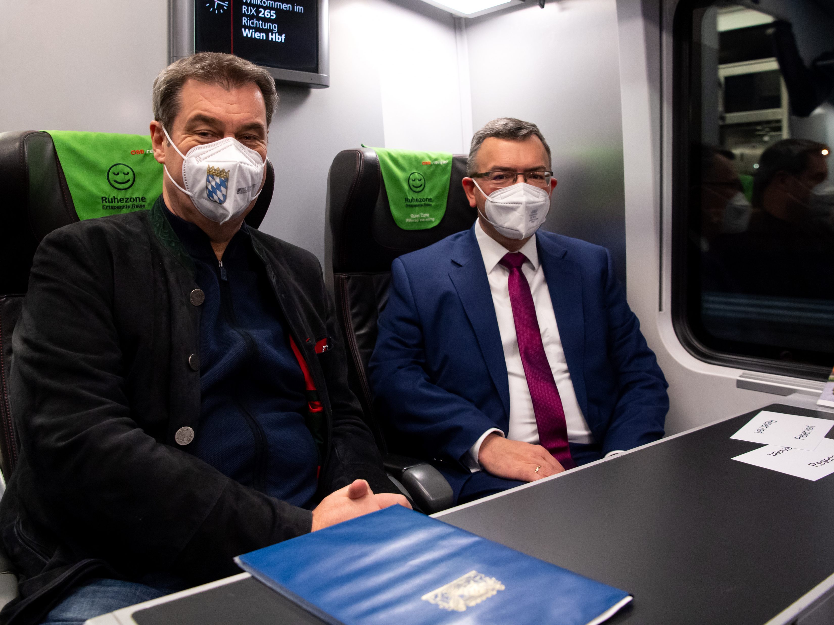 Markus Söder (l, CSU), Ministerpräsident von Bayern, und Florian Herrmann (CSU), Leiter der bayerischen Staatskanzlei, sitzen am Hauptbahnhof in einem Zug der ÖBB nach Wien. Söder will sich in Wien mit Bundeskanzler Nehammer und Innenminister Karner treffen.
