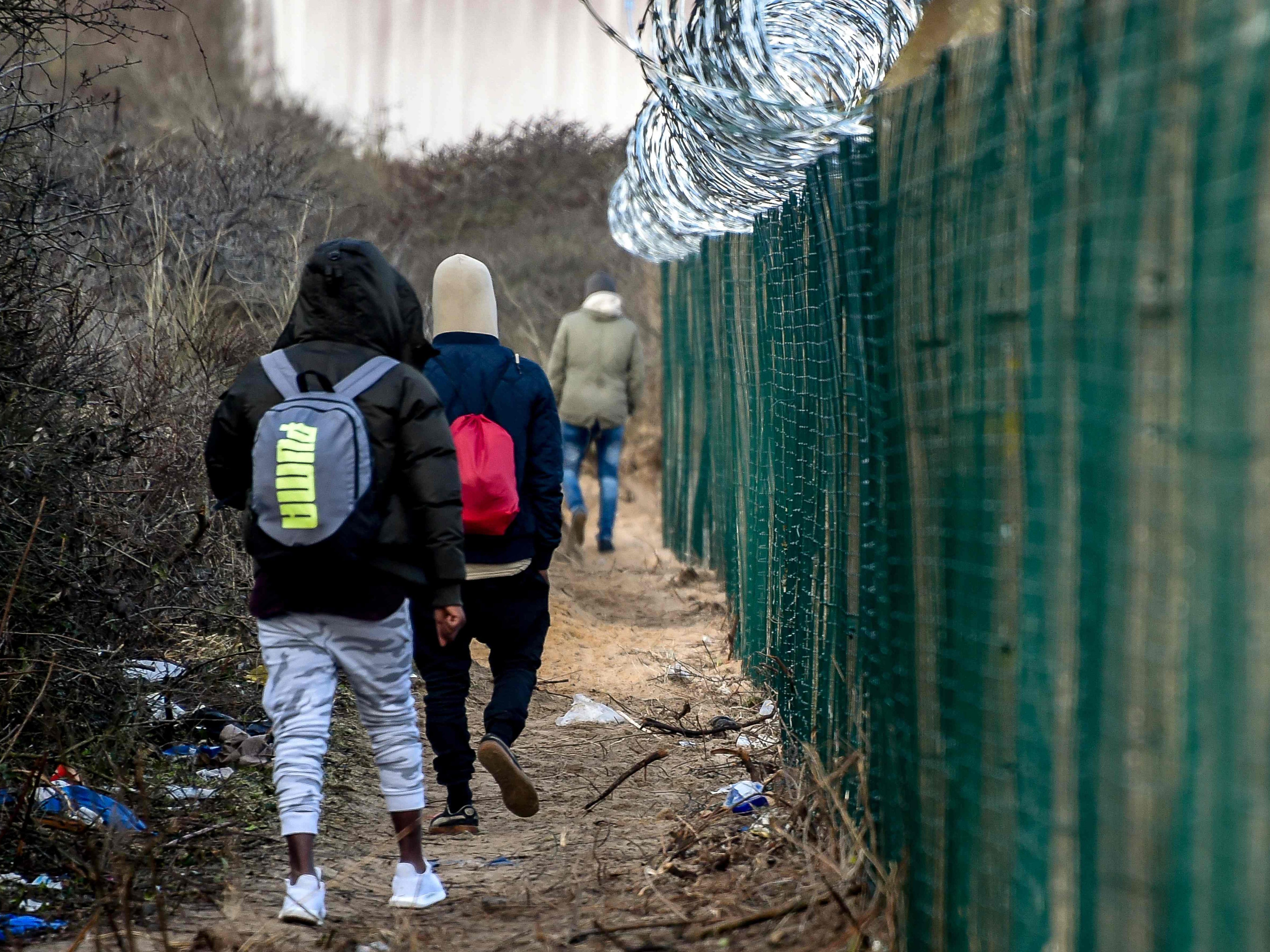 Flüchtlinge gehen entlang eines Grenzzauns bei Calais.