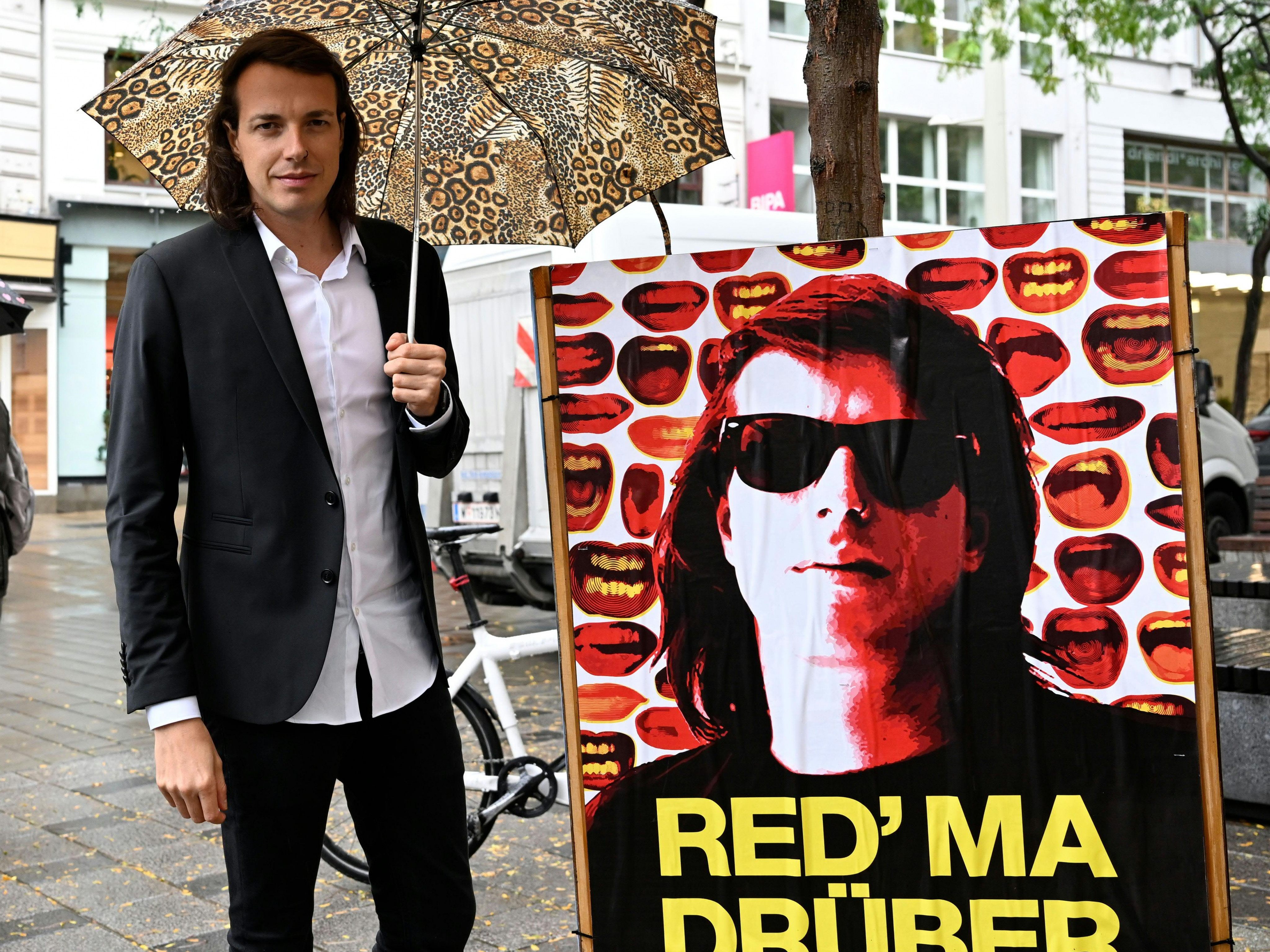 BP-Wahl: Kandidat Dominik Wlazny neben einem Plakat mit seinem Gesicht.