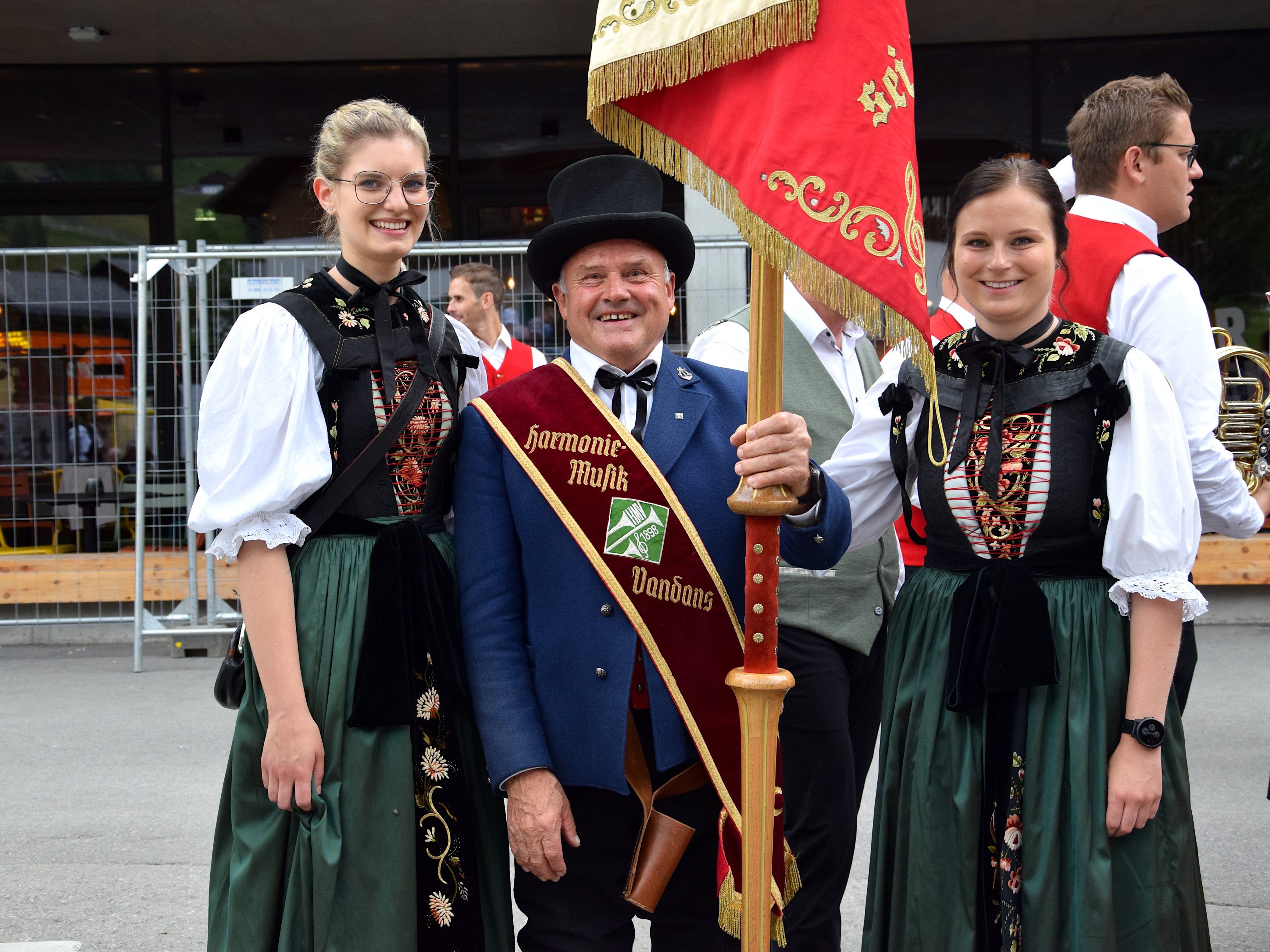 Alexandra Schwarz (l.) und Nadja Köberle, Marketenderinnen der Harmoniemusik Vandans, nahmen beim Musikfest in St. Gallenkirch Vereinsfähnerich Gerhard Bitschnau in ihre Mitte.