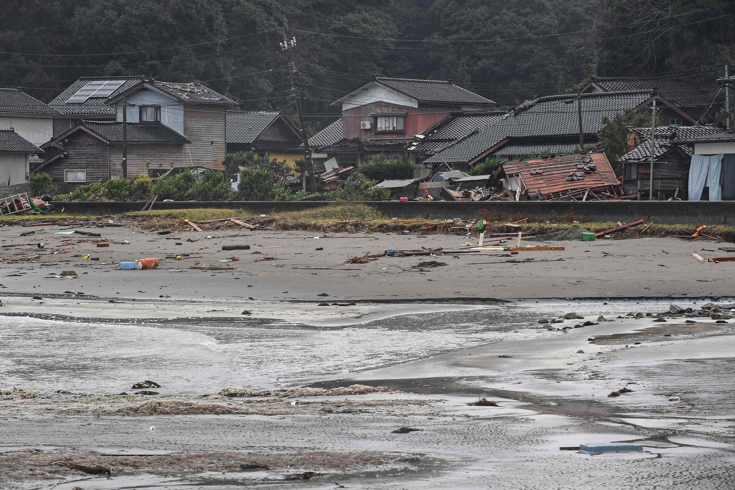 Dieses Bild zeigt Trümmer an einem Strand neben beschädigten Häusern in einem von Tsunamiwellen betroffenen Gebiet in der Stadt Misaki in der Stadt Suzu in der Präfektur Ishikawa am 7. Januar 2024 Dieses Bild zeigt Trümmer an einem Strand neben beschädigten Häusern in einem von Tsunamiwellen betroffenen Gebiet in der Stadt Misaki in der Stadt Suzu in der Präfektur Ishikawa am 7. Januar 2024