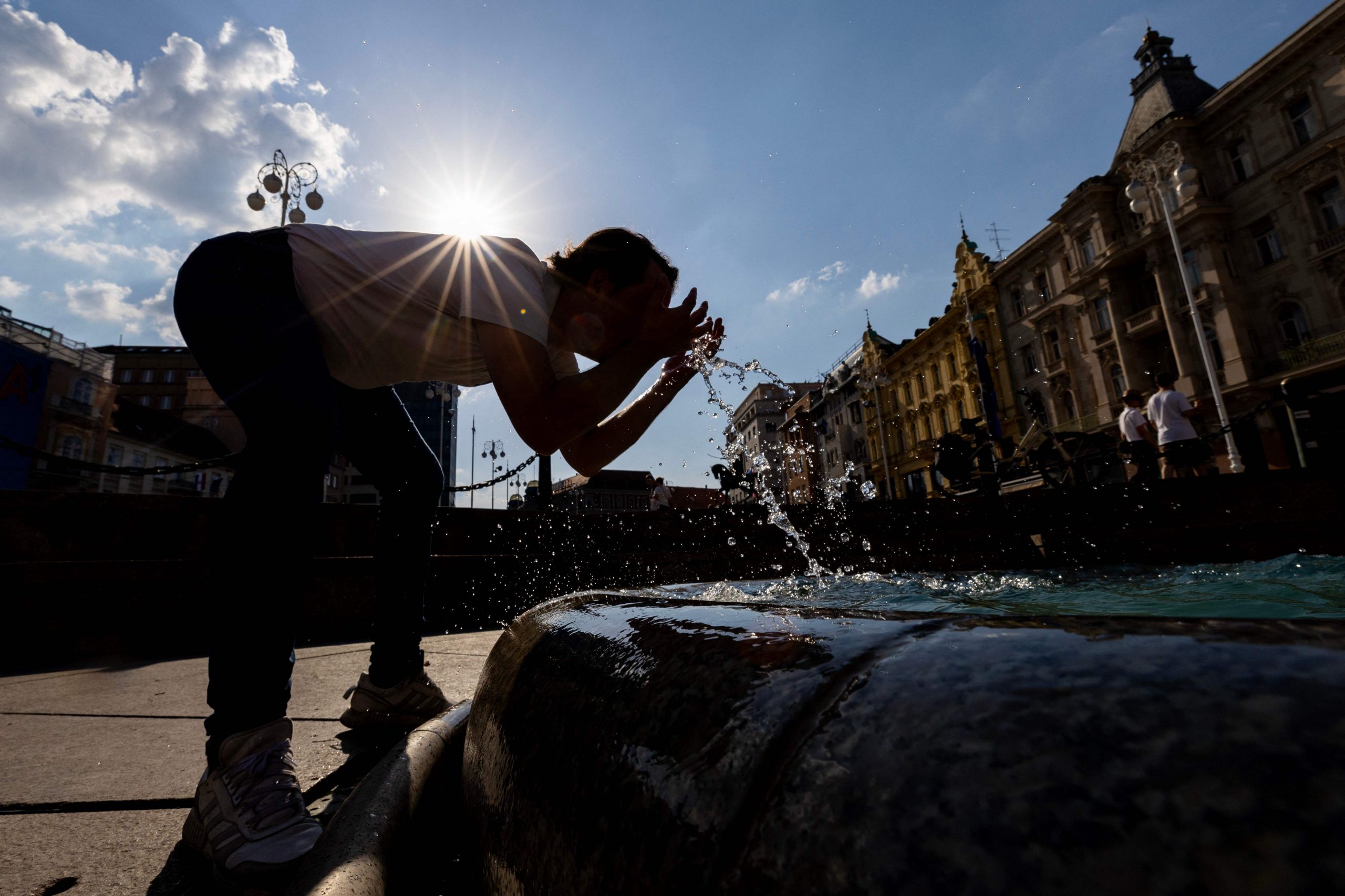 Ein Mann bespritzt sich mit Wasser aus einem Brunnen, um sich während einer Hitzewelle im Zentrum von Zagreb abzukühlen.