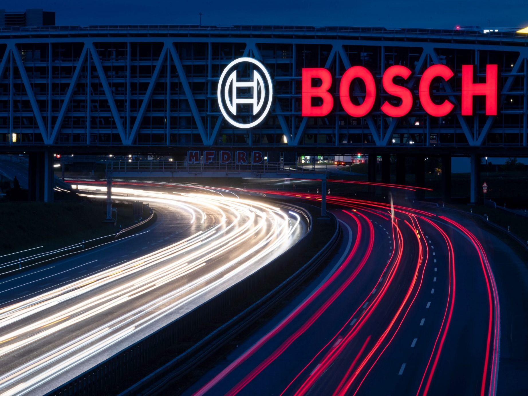 Das Logo des Technologiekonzerns Bosch leuchtet auf einem Parkhaus der Messe Stuttgart über der A8.