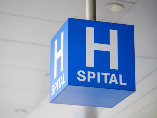 Auf dem Bild sieht man einen blauen Würfel mit der weißen Aufschrift Spital und darüber einem großen H. Es ist das Verkehrszeichen für Krankenhäuser.