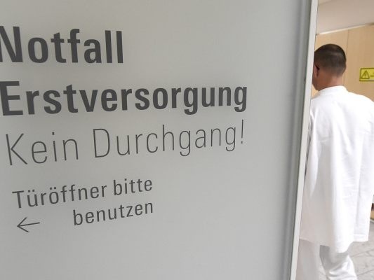 Auf dem Foto sieht man einen Hinweis in einem Spital, in welche Richtung es zur Notfall-Aufnahme geht. Neben dem Hinweis geht ein Arzt vorbei.