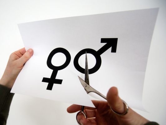 Auf dem Biild sieht man ein Blatt Papier mit den Symbolen für männlich und weiblich. Jemand schneidet mit einer Schere zwischen den Symbolen durch.