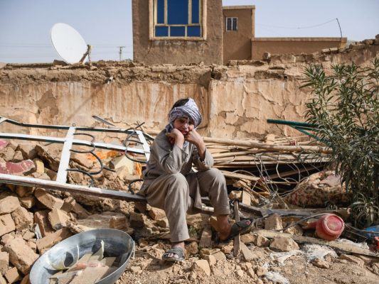 Auf dem Bild sieht man einen Mann auf den Trümmern von einem Haus sitzen.