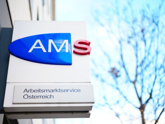 Auf dem Bild sieht man ein Schild vom AMS auf einer Hauswand.